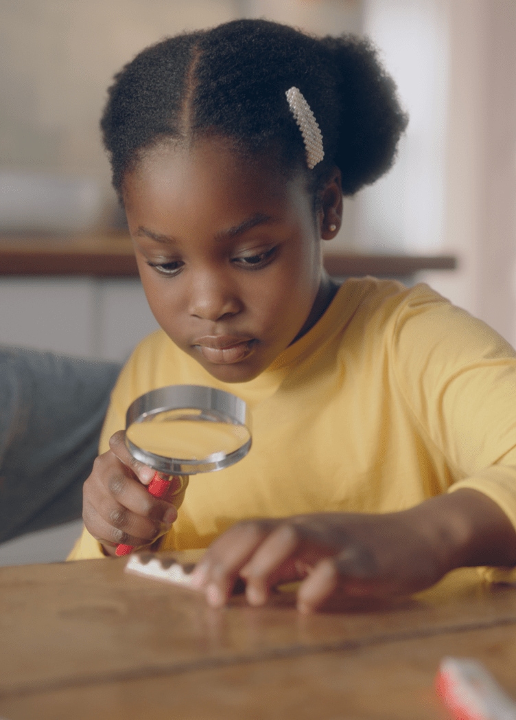 Young girl with magnifying glass and a kinder bar