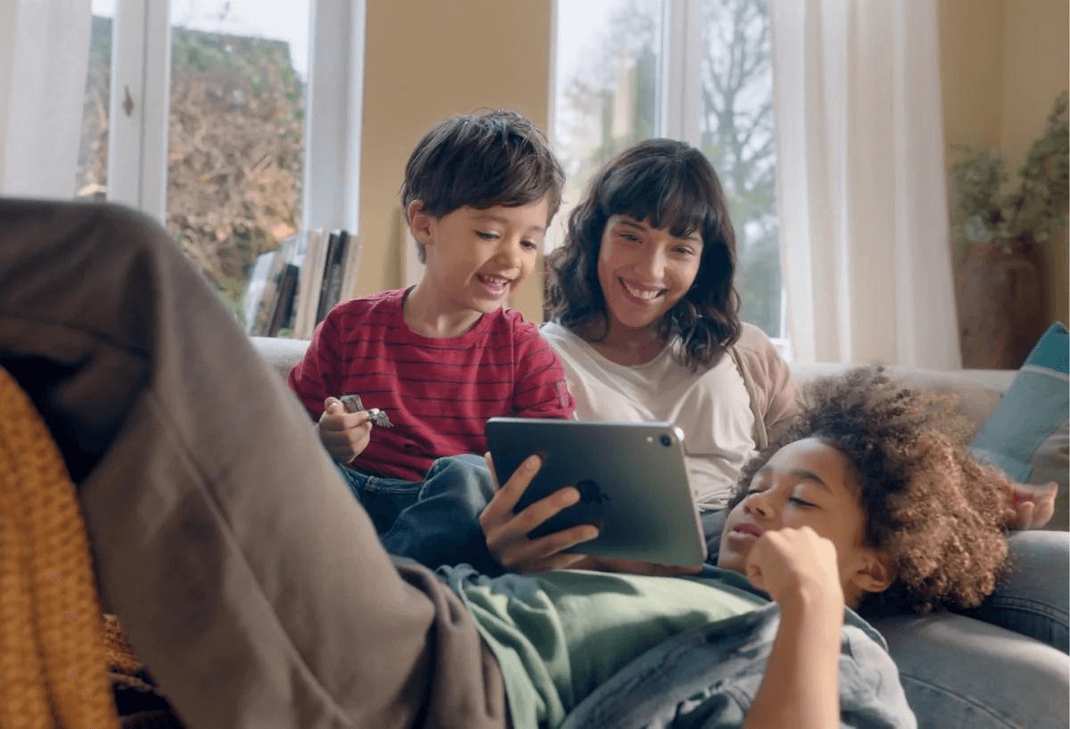 Dos niños jugando en un iPad con una mujer mayor Dos niños jugando en un iPad con una mujer mayor