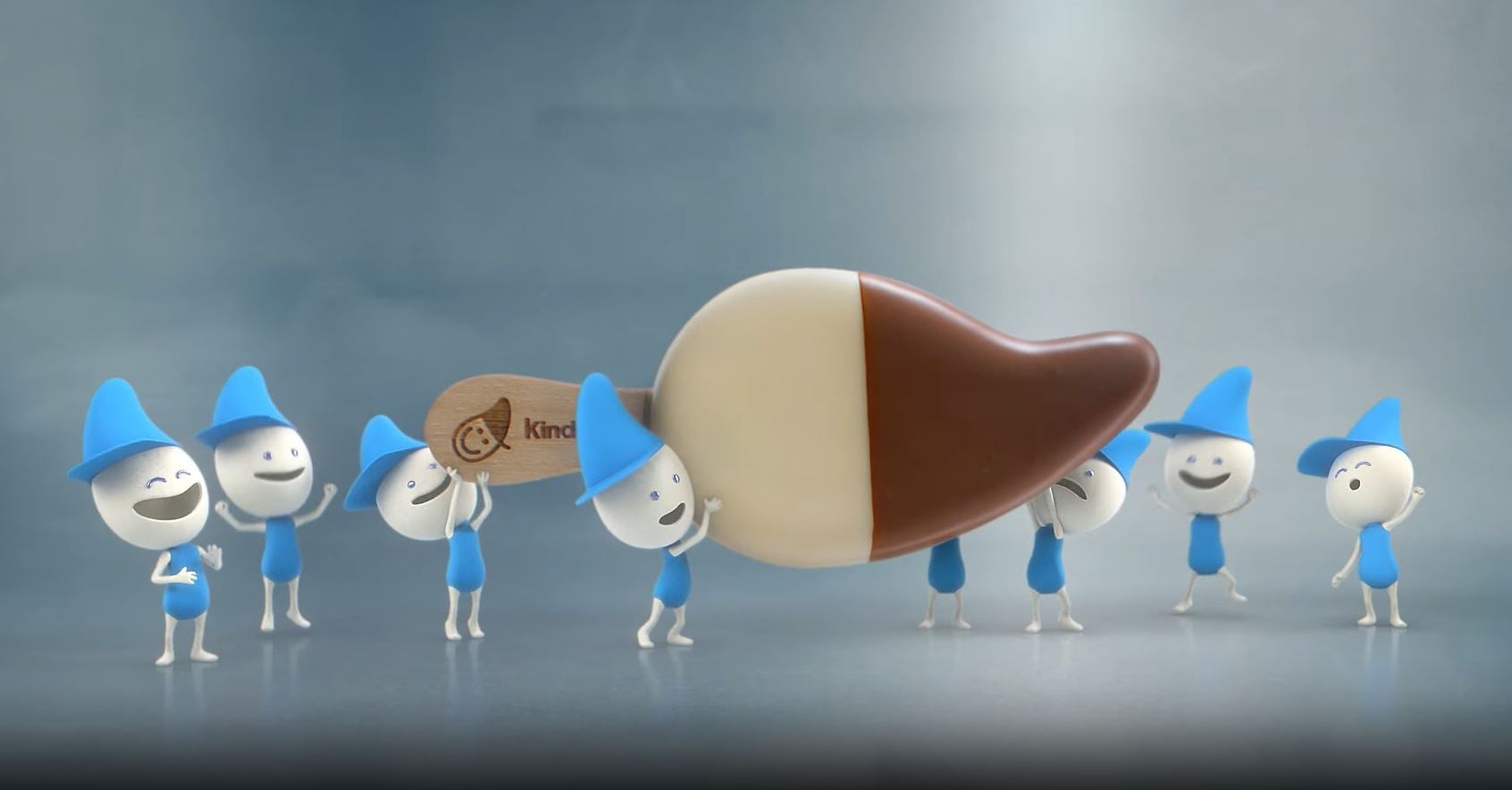 Piccoli Personaggi a forma di Goccia Kinder con cappelli blu trasportano insieme un enorme stecco gelato Kinder a forma di goccia metà al latte e metà al cacao.
