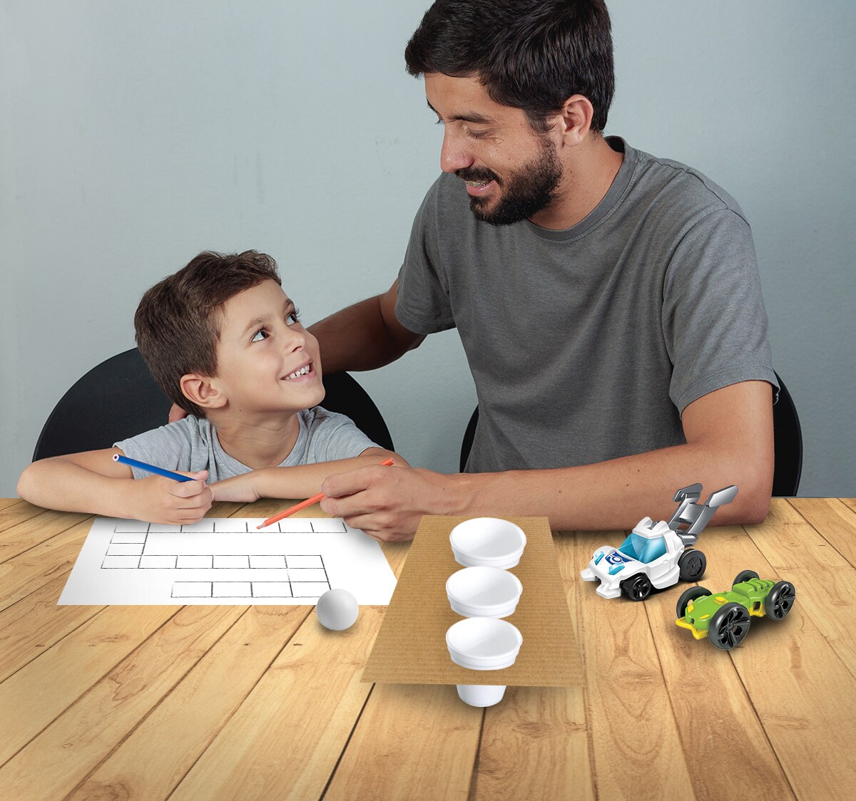 Papá y niño sonrientes haciendo manualidades sobre una mesa.