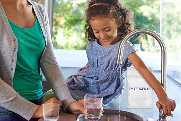 Mamá con hija llenando un vaso de cristal con agua del grifo en la cocina.