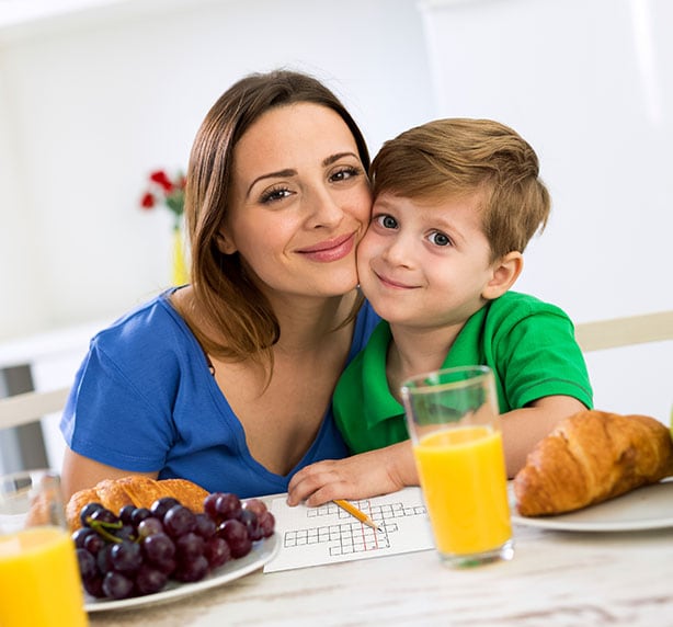 Mamá e hijo sonrientes desayunando y escribiendo sobre papel.
