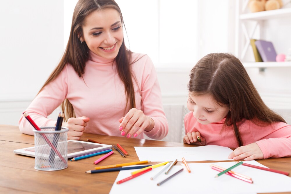 Mamá y niña realizando manualidades sobre una mesa con lápices de colores y hojas de papel